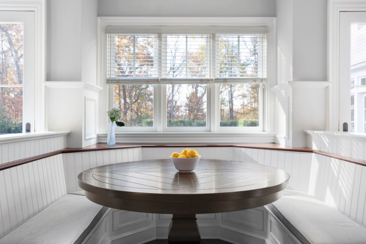 Faux wood blinds cover three side-by-side windows in a spacious breakfast nook.