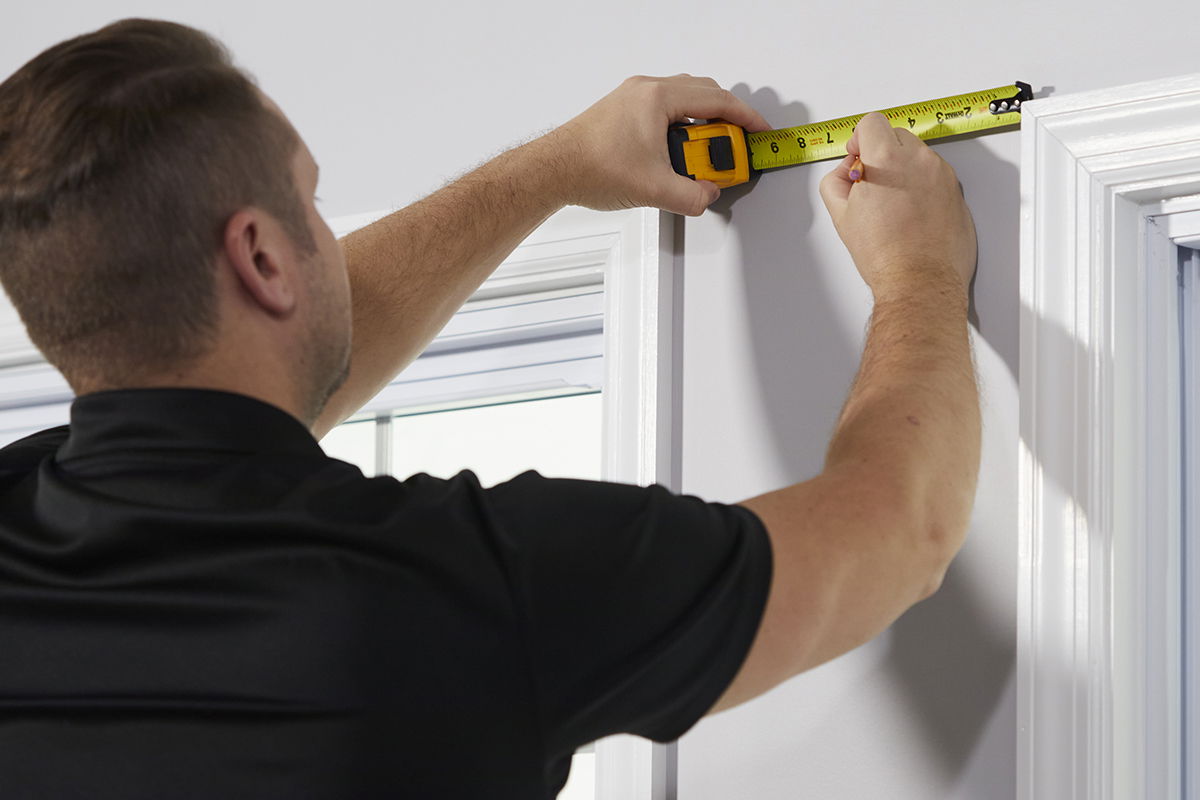 A measure technician measures the distance between two window frames.