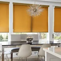 Roller shades in a rich gold color cover large windows in a modern dining room