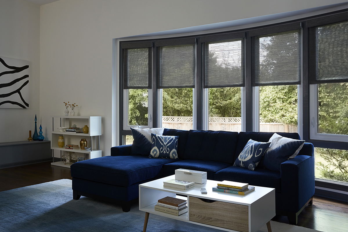 Solar shades cover a large bow window behind a large couch in a modern living room.